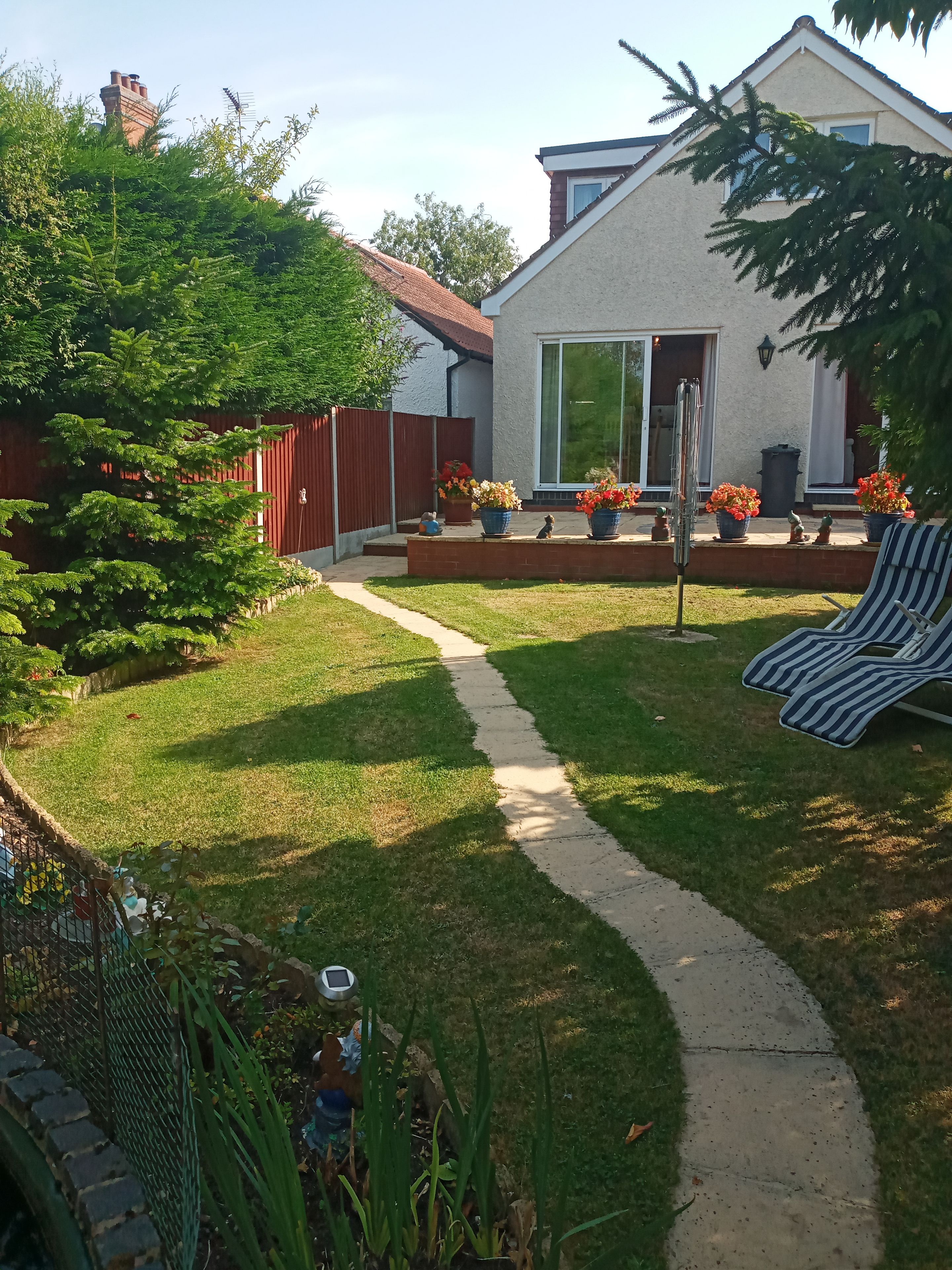 A backyard with a lawn, a pathway, a red fence, and a house with a white exterior.