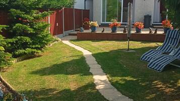A backyard with a lawn, a pathway, a red fence, and a house with a white exterior.