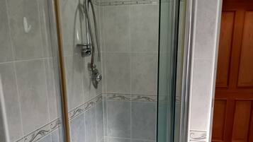 A glass-enclosed shower with a tiled wall and a wooden door in the background.