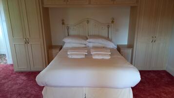 Una cama grande con ropa blanca, un cabecero con detalles decorativos y un suelo cubierto de alfombra roja.