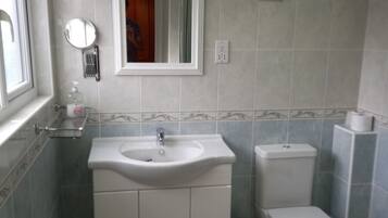 A bathroom with a sink, mirror, toilet, and a trash bin.