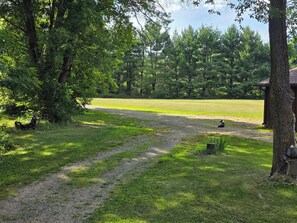 A grassy area with a dirt path leading to a building, surrounded by trees. - Private Home,1+acre property,close to WIDells/CastleRock,FirePit,yard games,wood (Adams)