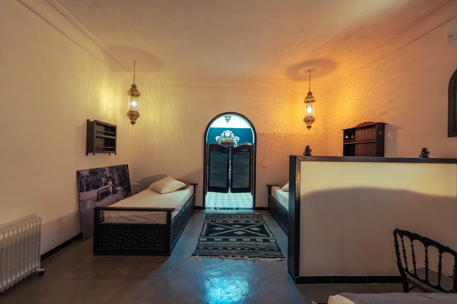 A room with a bed, a desk, a radiator, and a door leading to another room.