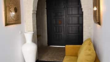 A hallway with a white vase, a yellow sofa, and a black door with a decorative archway.