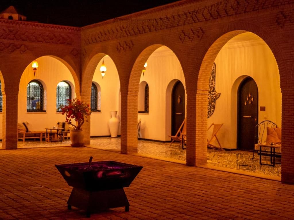 A courtyard with arched walkways, a central fire pit, and seating areas.