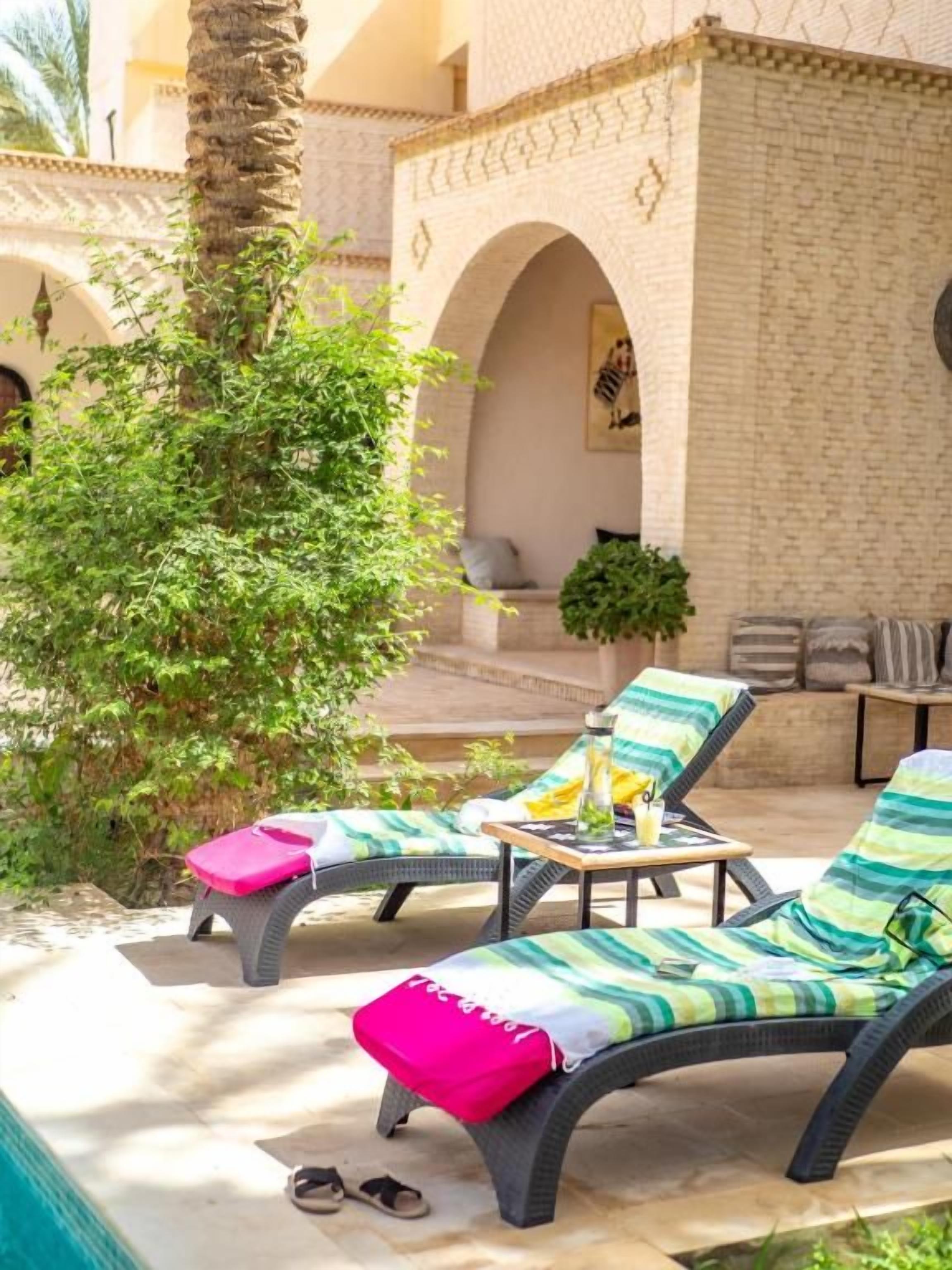 A sunlit outdoor lounge area with two lounge chairs, a small table, and a potted plant.