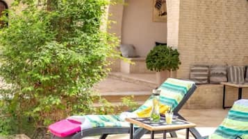 A sunlit outdoor lounge area with two lounge chairs, a small table, and a potted plant.