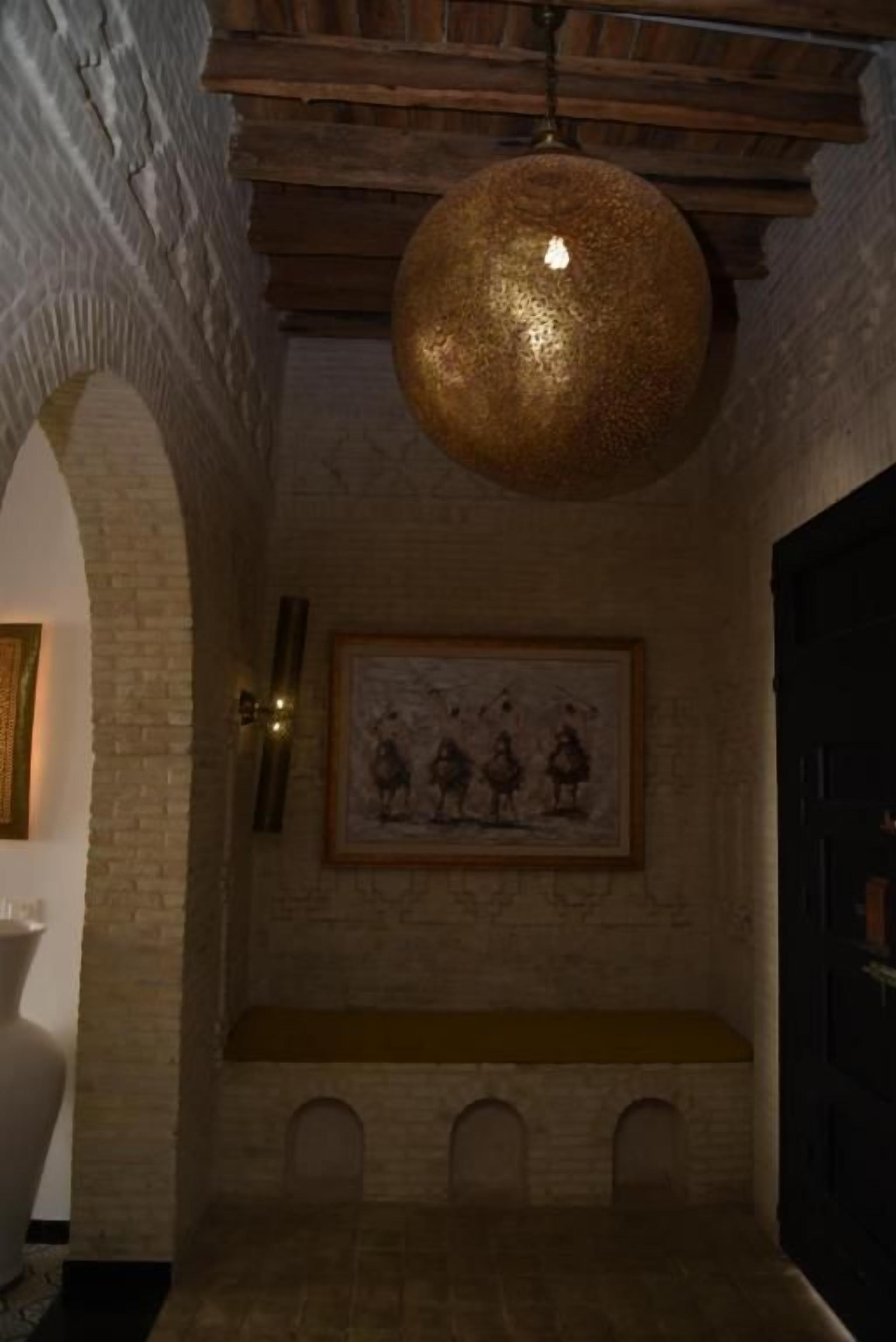 A room with a vaulted ceiling, a hanging spherical light fixture, a framed artwork on the wall, and a bench with a cushioned seat.