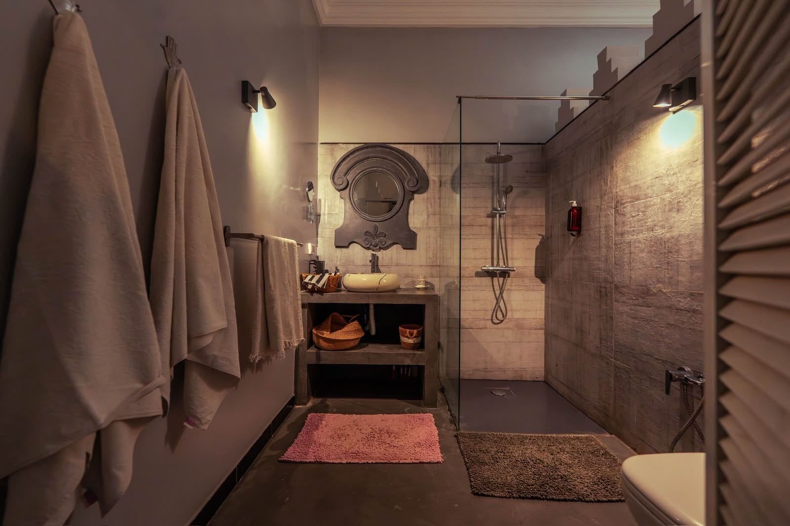 A modern bathroom with a glass shower enclosure, a sink with a mirror above, and towels on the wall.
