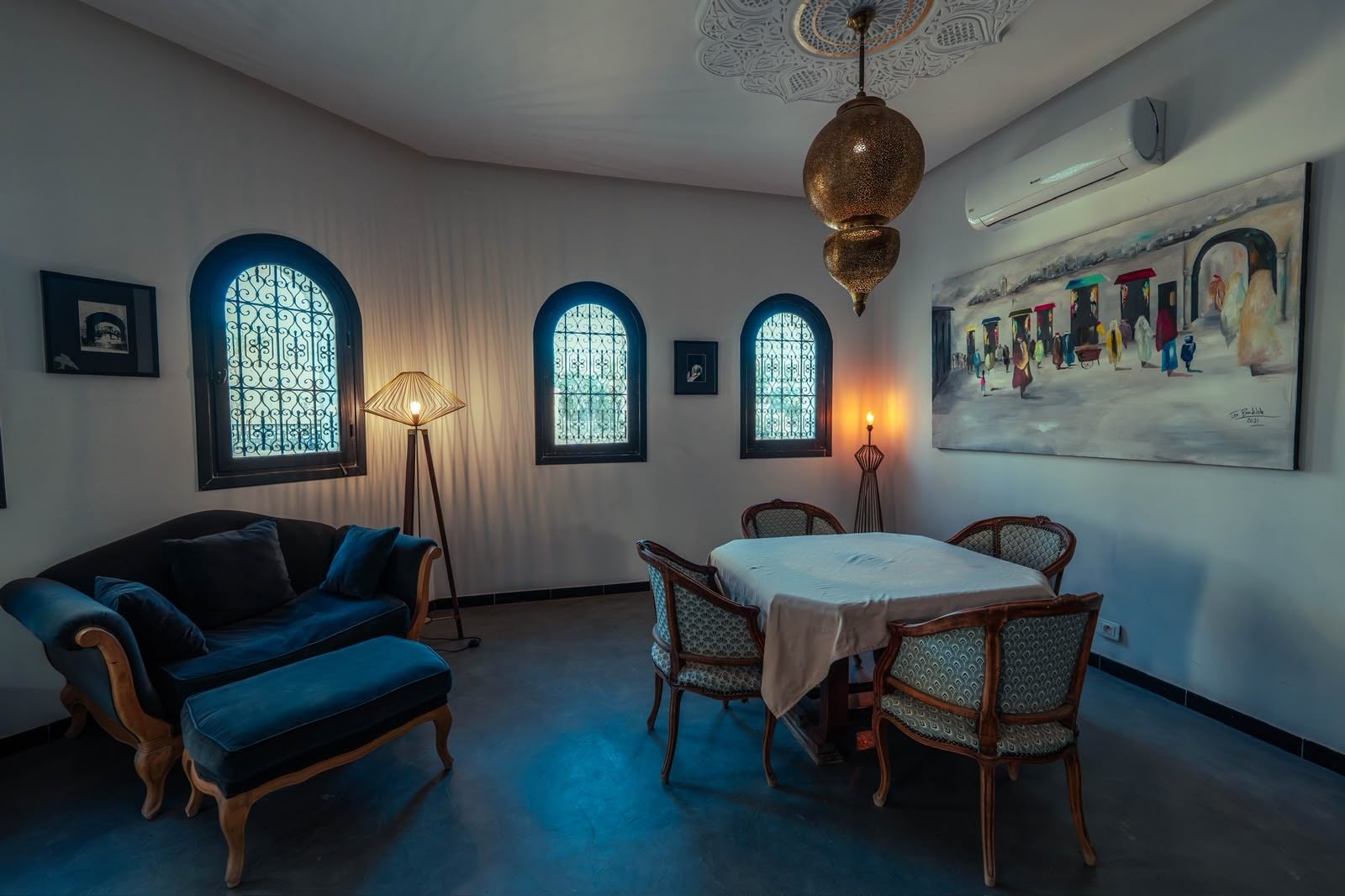 A room with a dining table, chairs, a sofa, and a large painting on the wall.