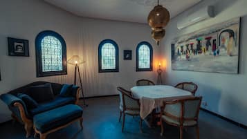 A room with a dining table, chairs, a sofa, and a large painting on the wall.