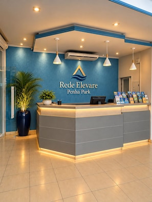 A reception desk with a logo, a plant, and brochures. - Rede Elevare Penha Park (Penha)