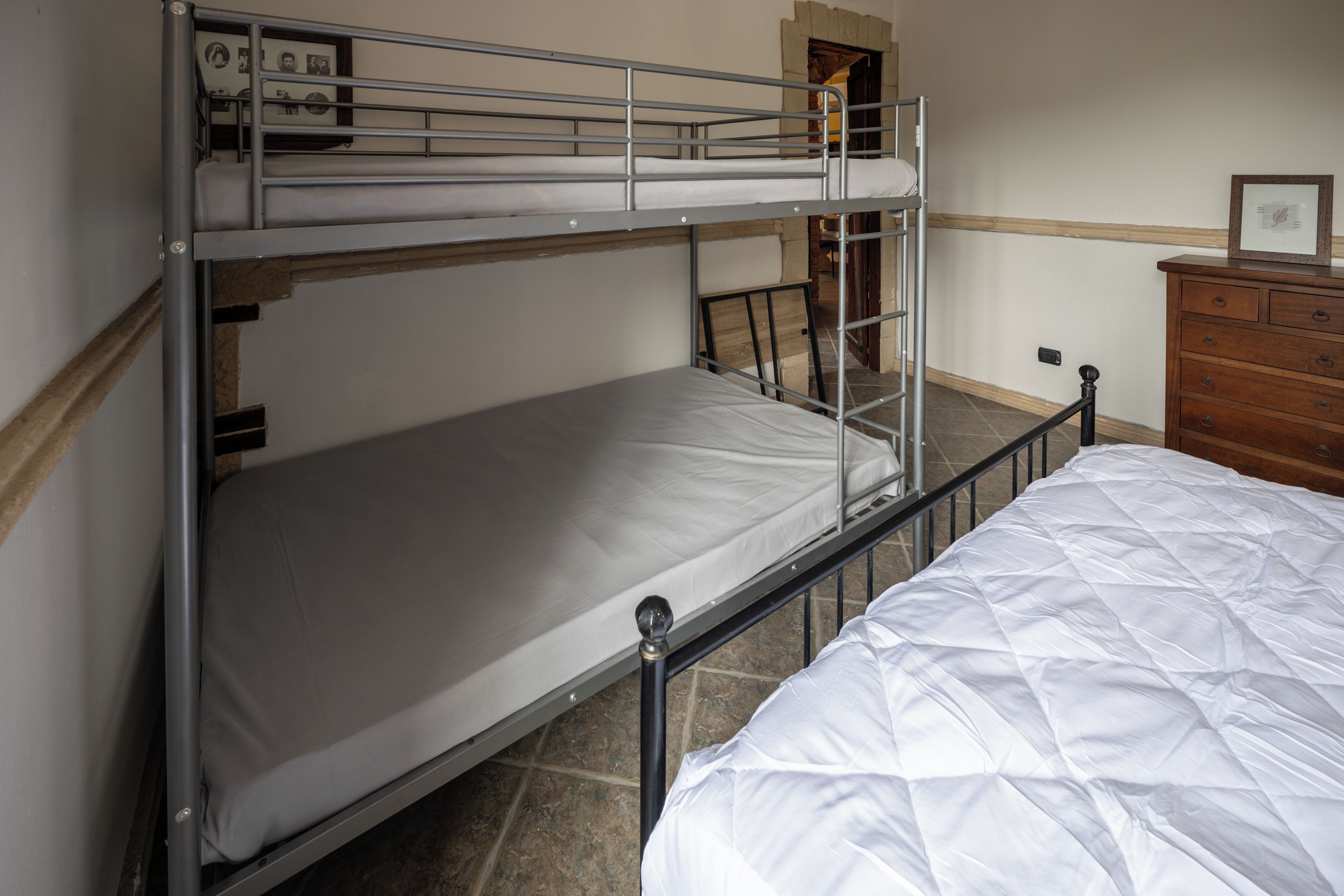 A bunk bed with a lower bunk, a wooden dresser, and a framed picture on the wall.