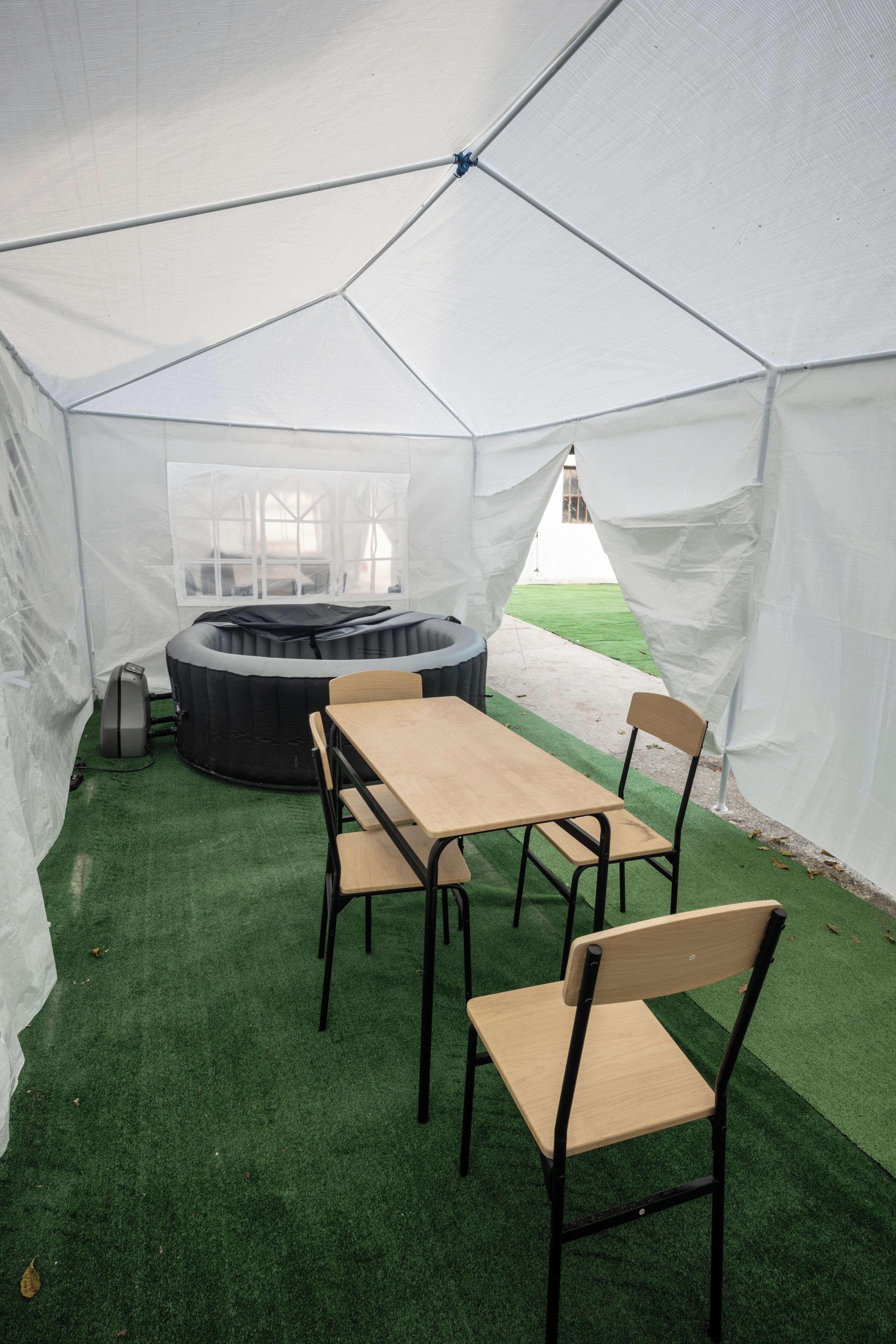 A tent with a table and chairs, a hot tub, and a grassy area outside.