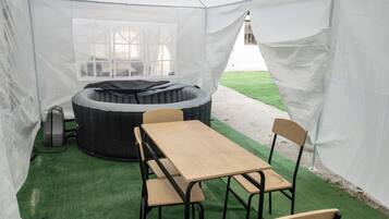 A tent with a table and chairs, a hot tub, and a grassy area outside.