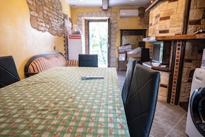 Un comedor con una mesa cubierta por un mantel a cuadros, sillas, un televisor y una lavadora.