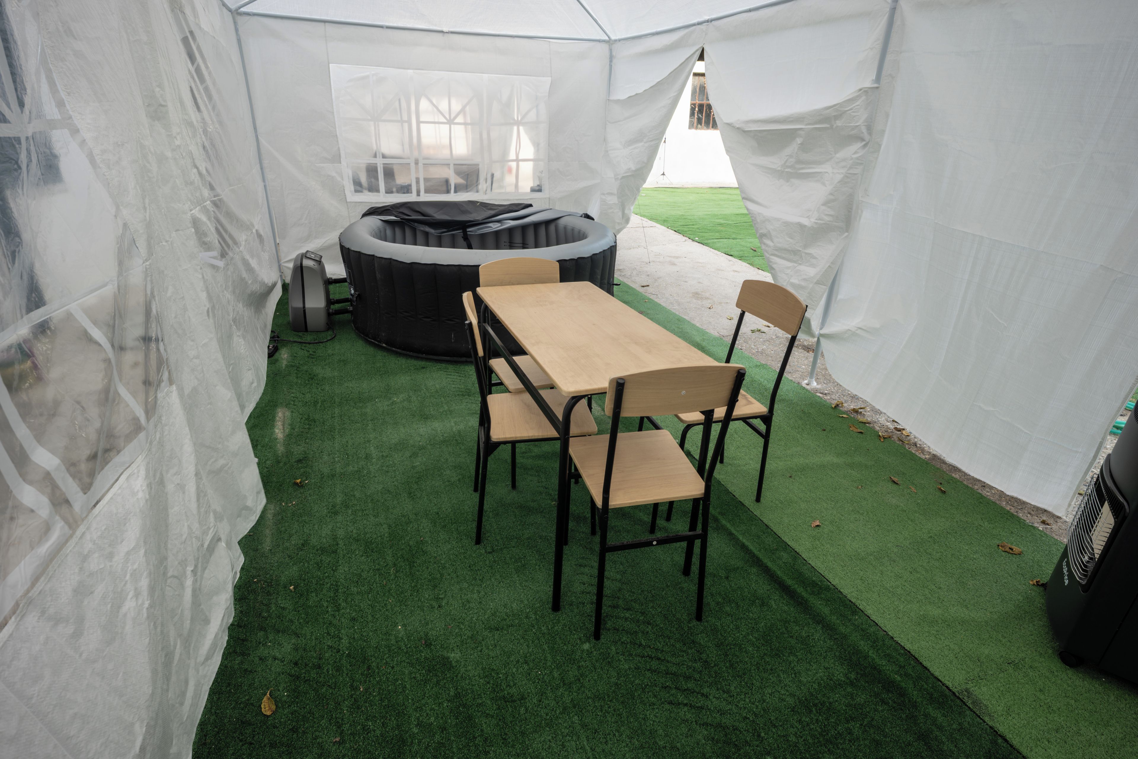 Una carpa con mesa y sillas, un jacuzzi y piso de césped artificial.