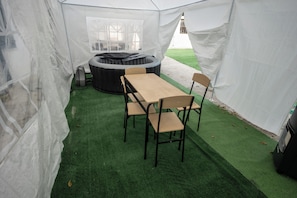 Una carpa con mesa y sillas, un jacuzzi y piso de césped artificial.