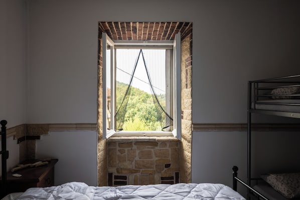 A bedroom with a bunk bed, a window with a view of greenery, and a stone wall.