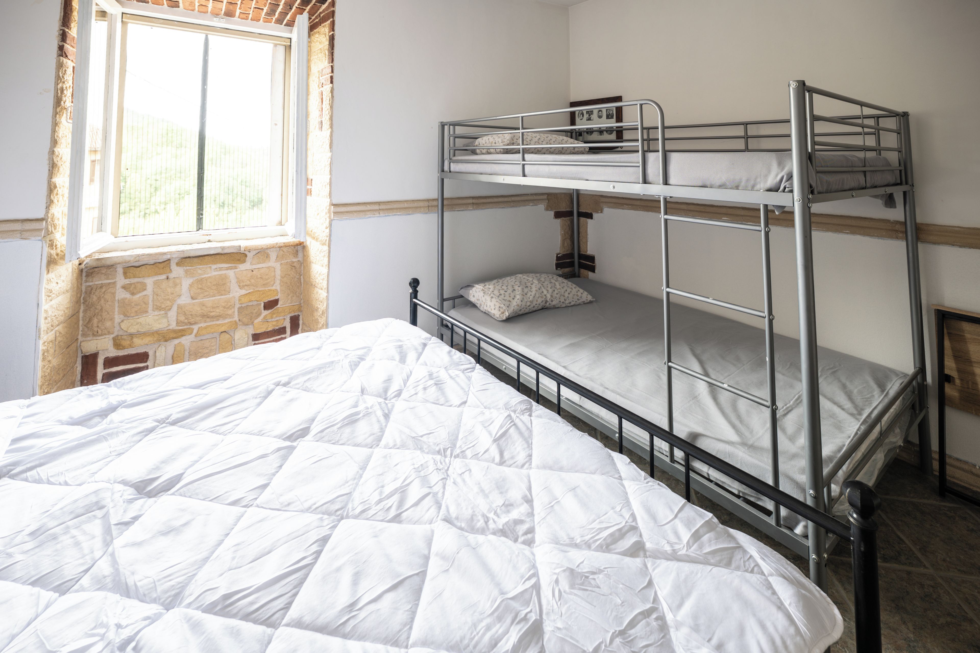 A bunk bed room with a window, stone wall, and a bed with a white quilt.