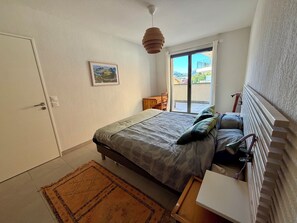Ein Schlafzimmer mit einem Bett, einem Schreibtisch, einem Stuhl, einer Heizung und Blick ins Freie.