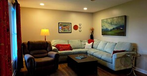 Ein Wohnzimmer mit einem braunen Ledersessel, einem hellgrauen Sofa, einem Couchtisch und einem Bild an der Wand.