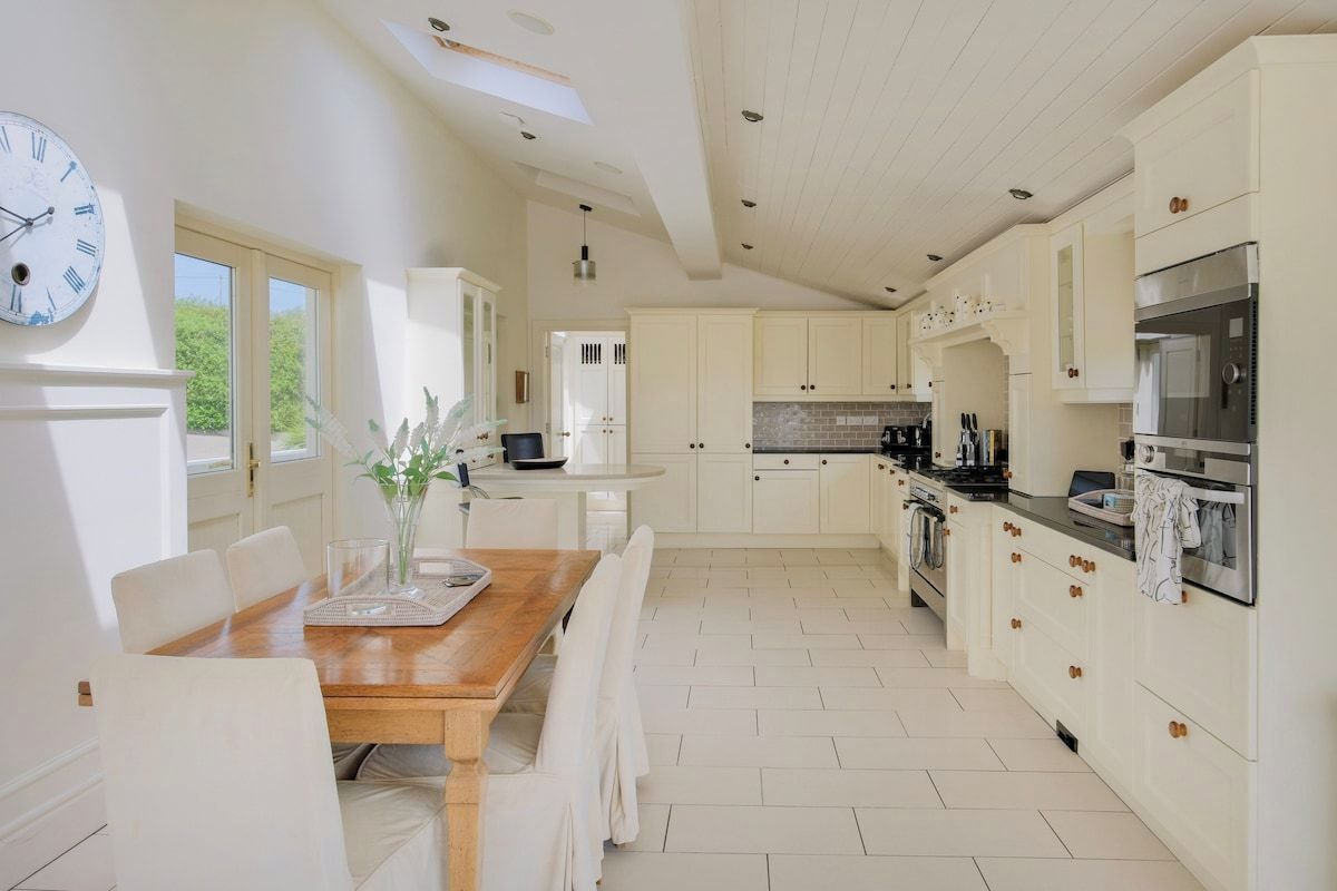 A spacious kitchen with white cabinetry, a wooden dining table, and a clock on the wall.