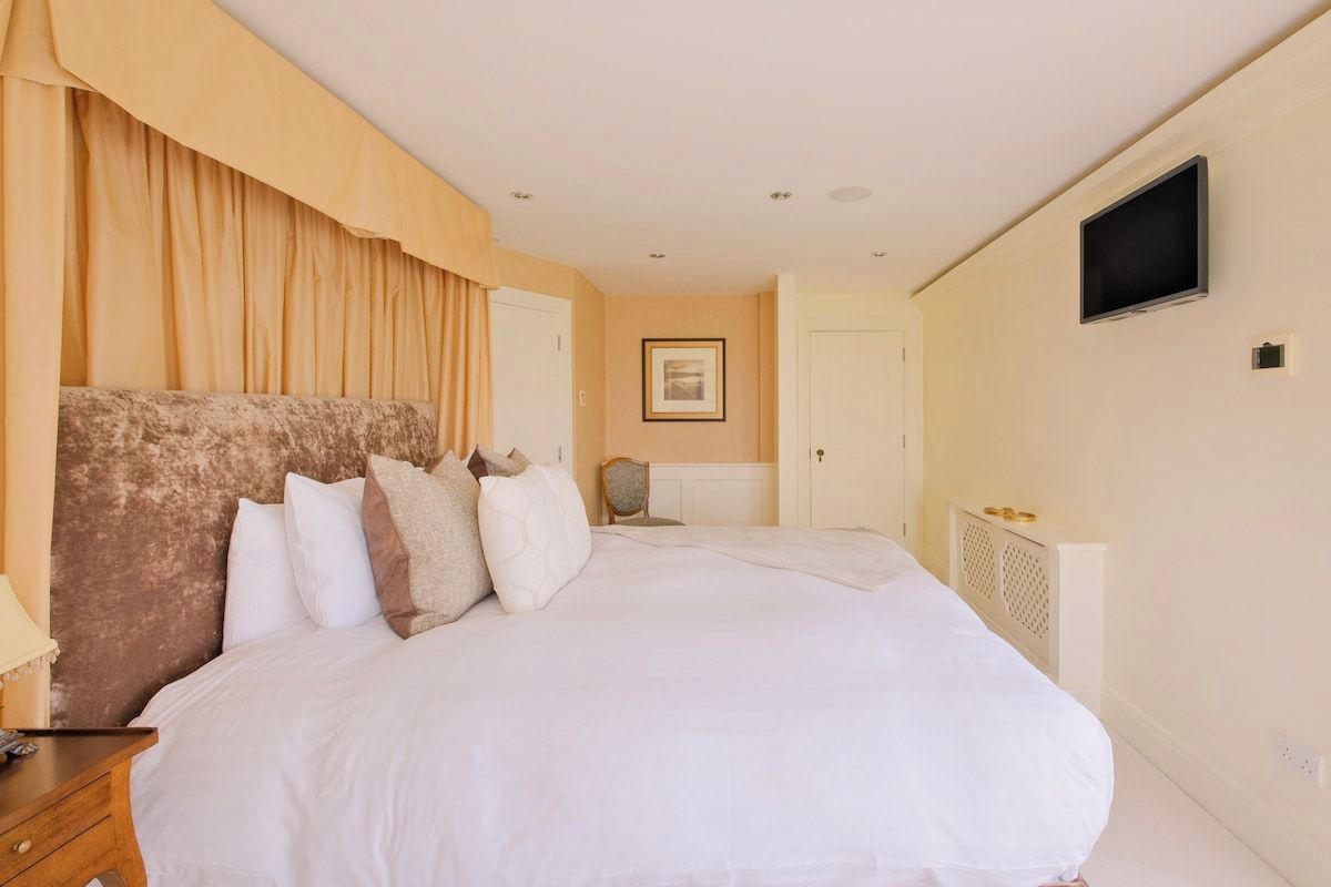 A hotel room with a large bed, a bedside table, a chair, a television, and a framed picture on the wall.
