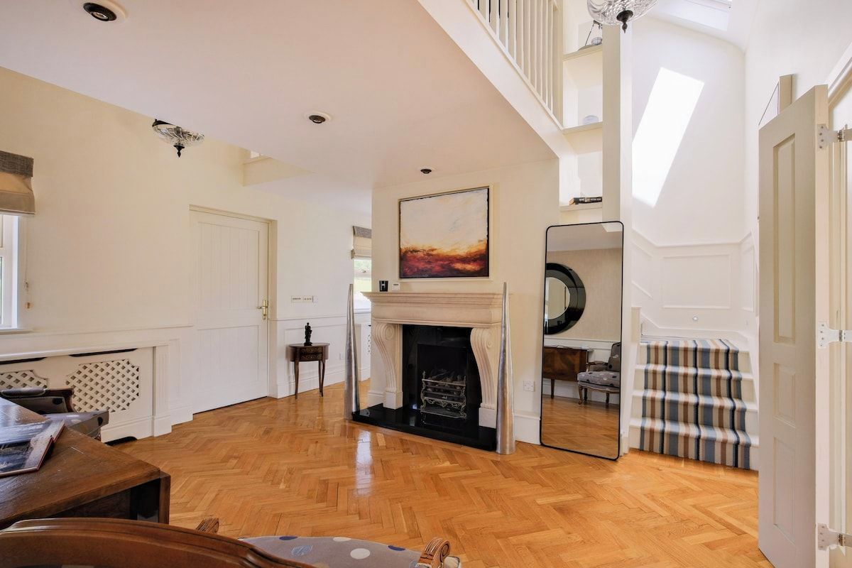 A spacious living room with a fireplace, wooden flooring, and a staircase leading to an upper level.