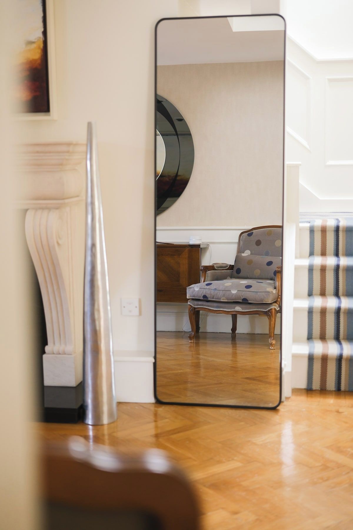 Una habitación con un espejo grande que refleja una silla y un sofá estampado.