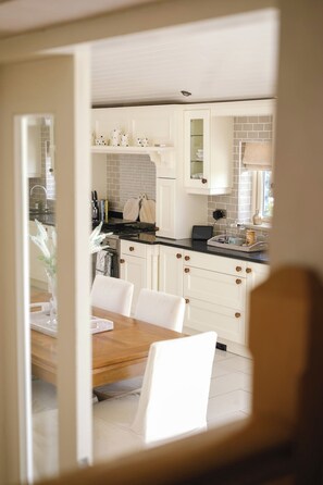 A modern kitchen with white cabinetry, a wooden dining table, and a view into the dining area. - Luxury Self-catering Home near Lahinch Golf Club - Howards Way Liscannor (Liscannor)