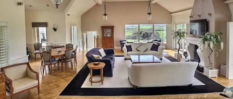 A spacious living area with a high ceiling, a fireplace, and a large window overlooking a scenic landscape.