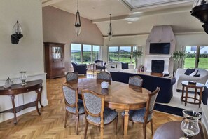 A spacious living room with a large wooden dining table, comfortable seating, a fireplace, and a view of the outdoors. - Luxury Self-catering Home near Lahinch Golf Club - Howards Way Liscannor (Liscannor)