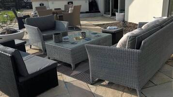 Un patio al aire libre con mobiliario de mimbre, una chimenea y vistas de la casa.