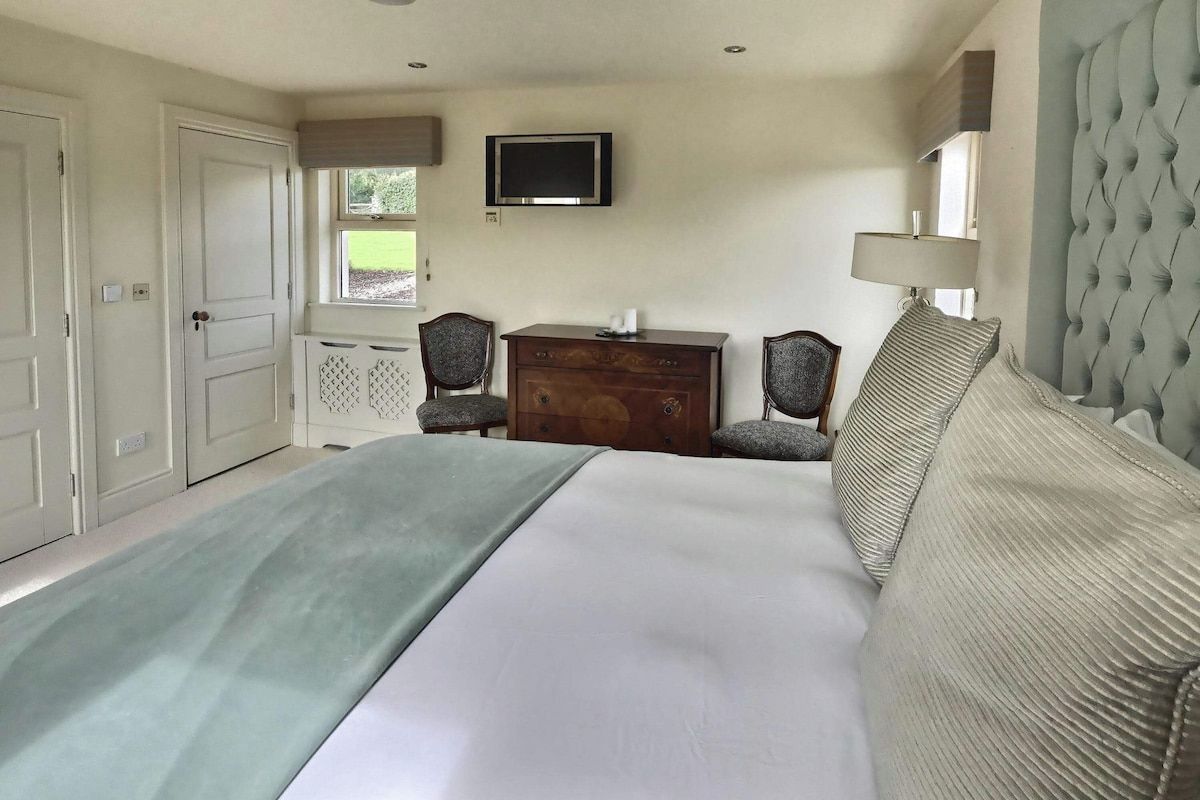 Een slaapkamer met een bed, een dressoir, een televisie en twee stoelen.