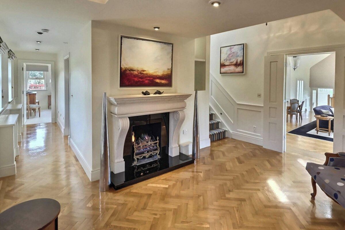 A spacious living room with a fireplace, hardwood flooring, and a staircase leading to another level.