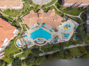 An aerial view of a resort with a central swimming pool, sun loungers, and a circular water feature. - Designer Luxury 3BR, Stunning Lake View, Vista Cay (Orlando)