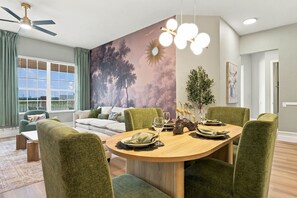 A dining area with a round wooden table, green upholstered chairs, and a mural of trees on the wall. - Designer Luxury 3BR, Stunning Lake View, Vista Cay (Orlando)