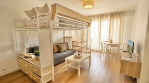 A compact living space with a bunk bed, a sofa, a dining table, and a TV. - Renovated apartment with a terrace and parking (Houlgate)
