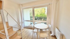A room with a wooden staircase, a round table with chairs, and large windows with a view of greenery outside. - Renovated apartment with a terrace and parking (Houlgate)