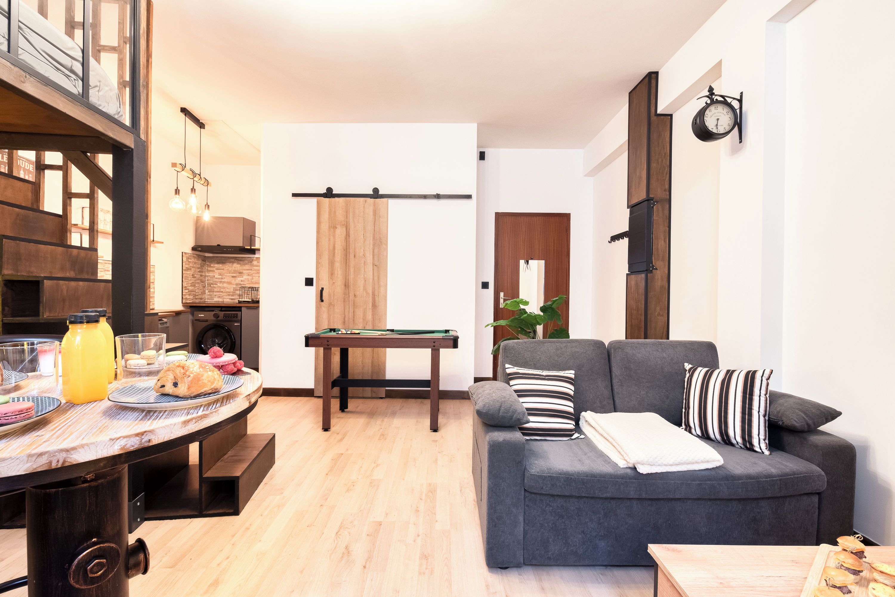 Ein modernes Wohnzimmer mit Billardtisch, einer Couch und einem Essbereich mit gedecktem Tisch.
