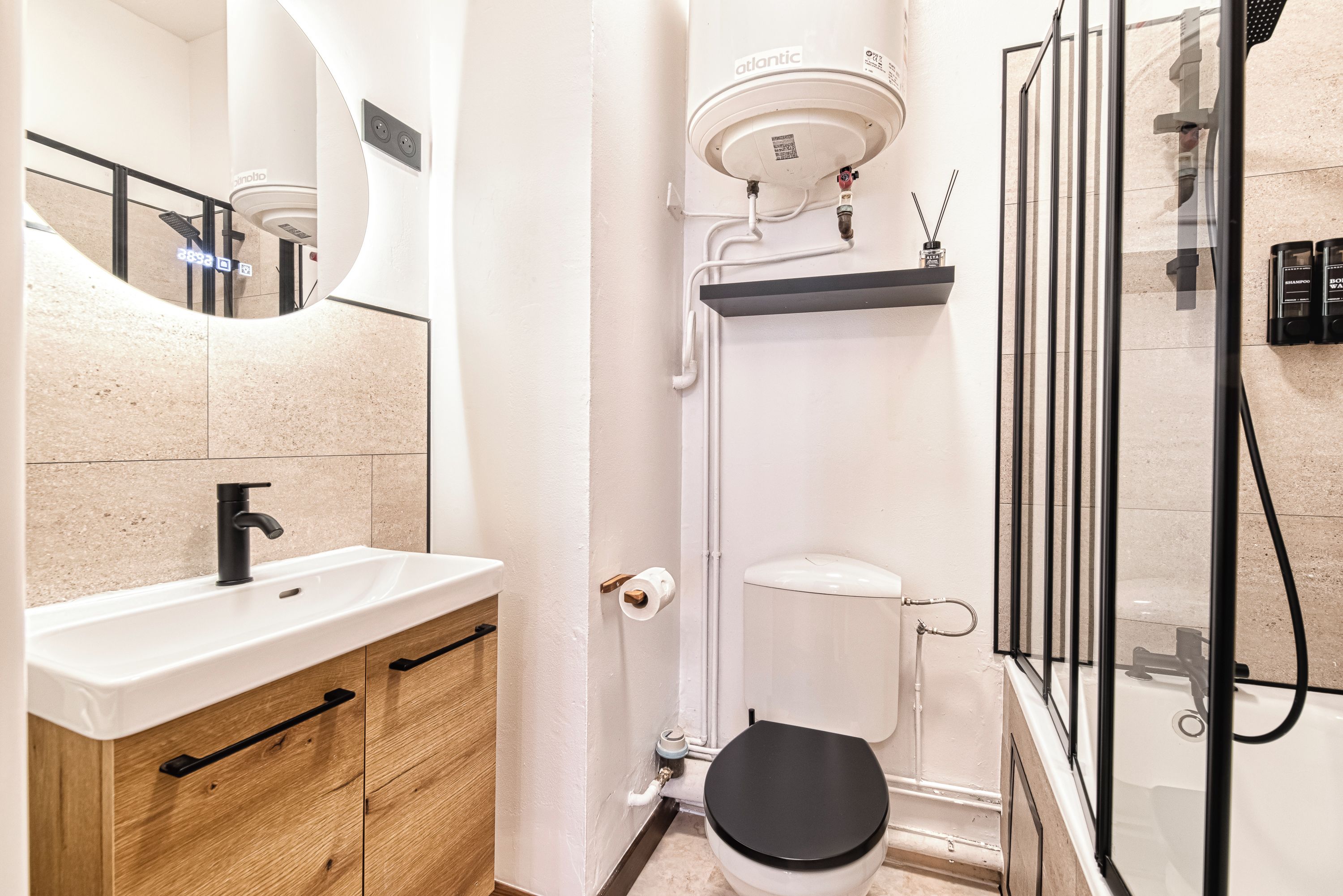 Ein modernes Badezimmer mit einem weißen Waschbecken, einem Holzschrank, einer Toilette und einer Duschkabine aus Glas.