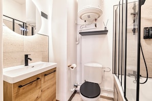Ein modernes Badezimmer mit einem weißen Waschbecken, einem Holzschrank, einer Toilette und einer Duschkabine aus Glas.