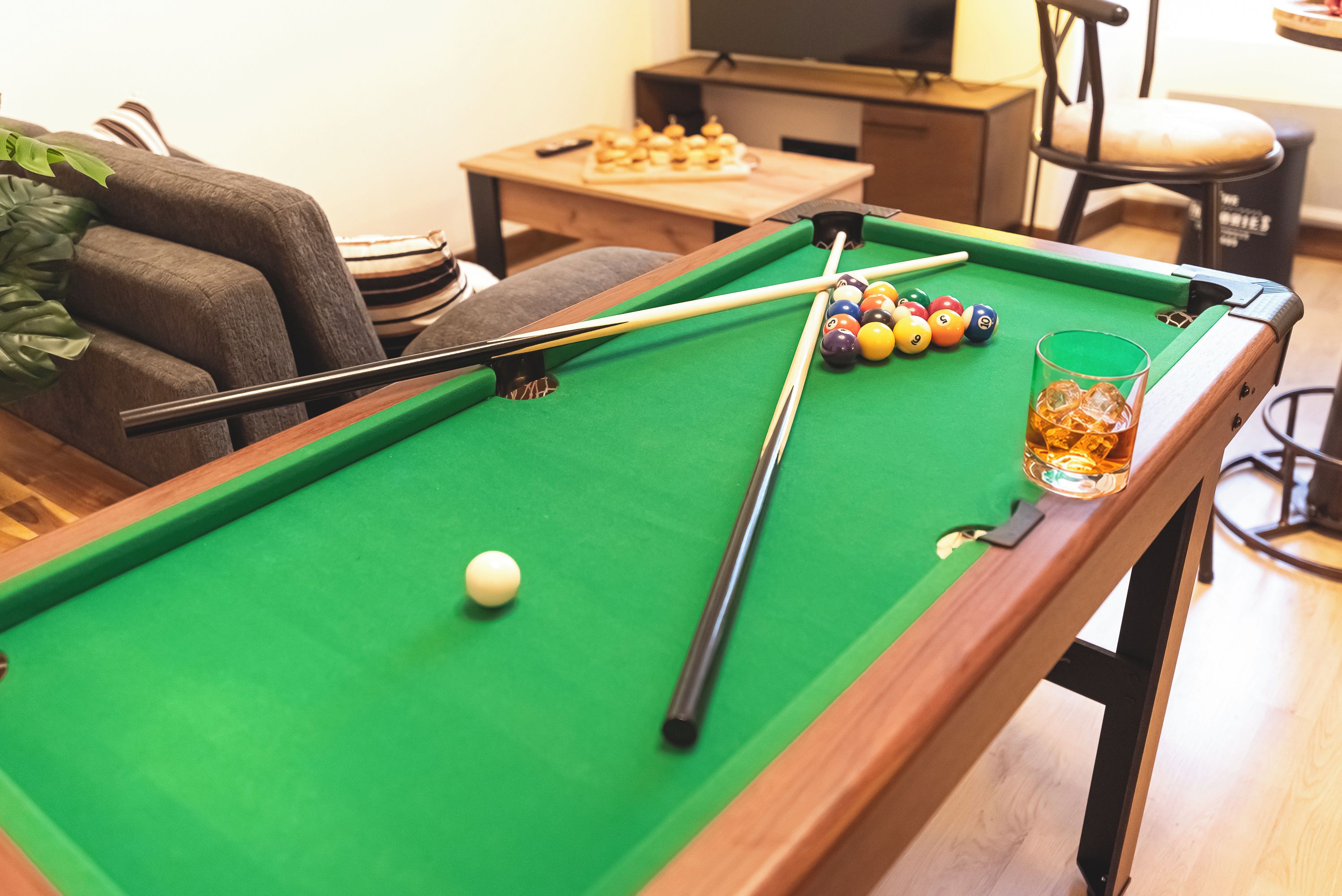 A pool table with balls, a cue stick, and a glass of beer.