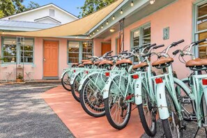 Una hilera de bicicletas numeradas estacionadas frente a un edificio con fachada rosa y un acceso cubierto.