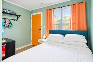 Un dormitorio con cama, mesita de noche, puerta y ventana con cortinas.