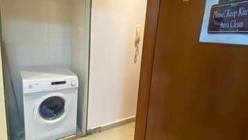 A hotel bathroom with a white washing machine, a glass shower enclosure, and a sign requesting to keep the area clean.