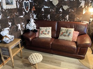 Ein braunes Ledersofa mit zwei Zierkissen, einem kleinen runden Hocker und einem Holztisch mit einem Korb.