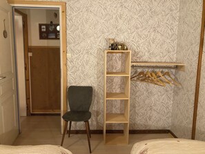 Ein Zimmer mit einem Sessel, einem Holzbodenregal, einem Kleiderhaken und einem Bett.