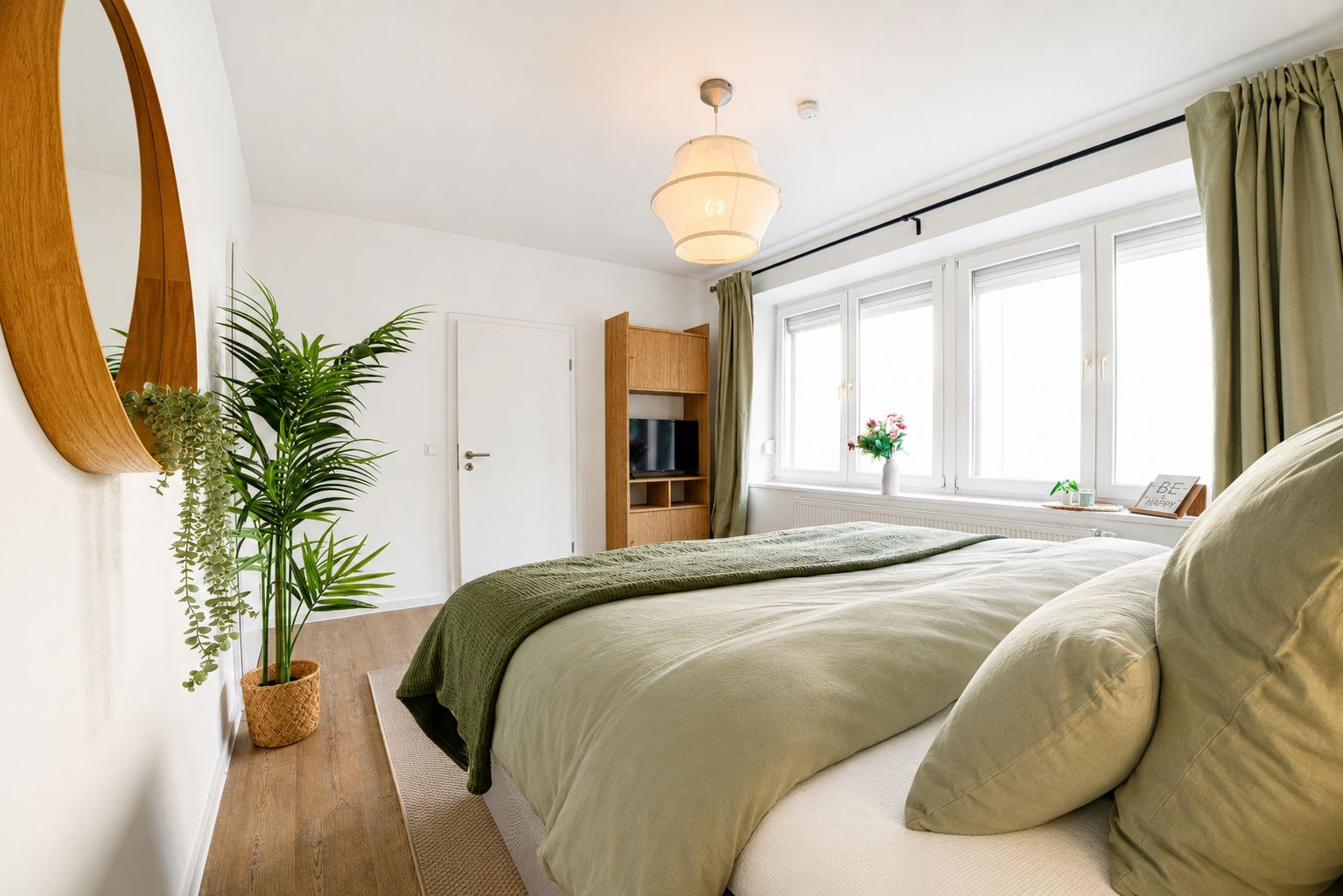 Ein Schlafzimmer mit Bett, Fernseher, Fenster mit Vorhängen und einer Topfpflanze.